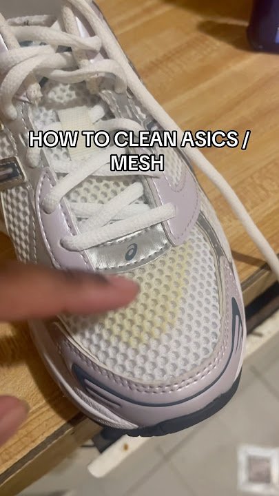 Person cleaning ASICS running shoes by hand with a soft brush and mild soap on a countertop.