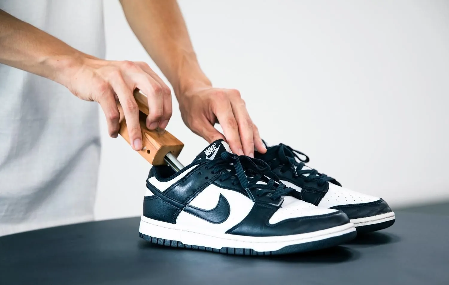 Step-by-step cleaning black suede Jordan sneakers with suede brush, eraser, and mink oil on a wooden table.