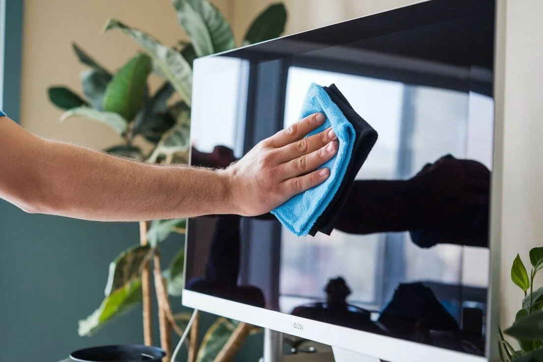 Close-up of a person cleaning an iMac screen with a soft microfiber cloth, showing gentle straight wiping motion