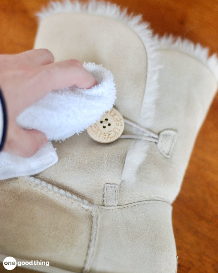 Wire brush fluffing cleaned sheepskin interior of Ugg boots with baking soda and cornstarch on wooden table