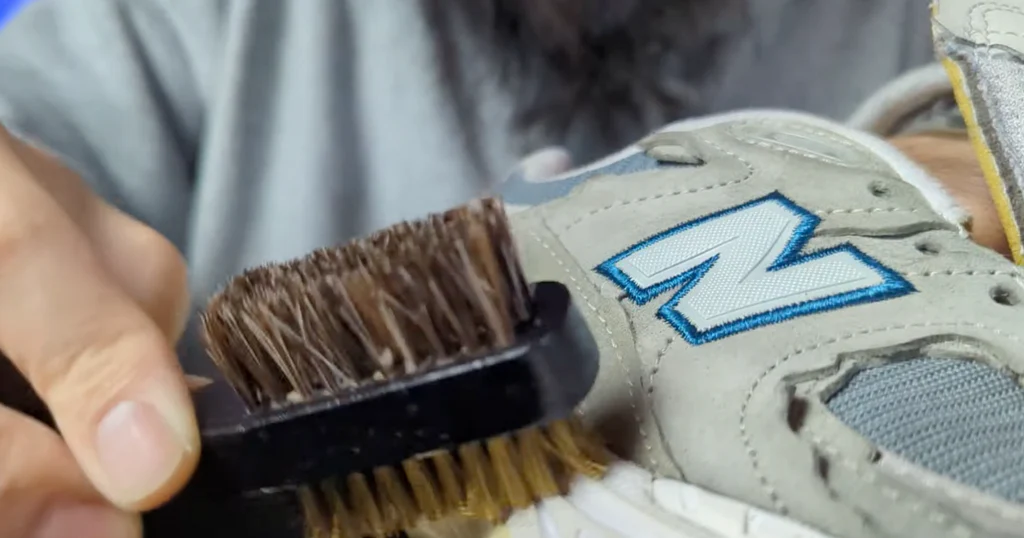Cleaning New Balance suede shoes step-by-step with suede brush, eraser, and vinegar on a workbench.