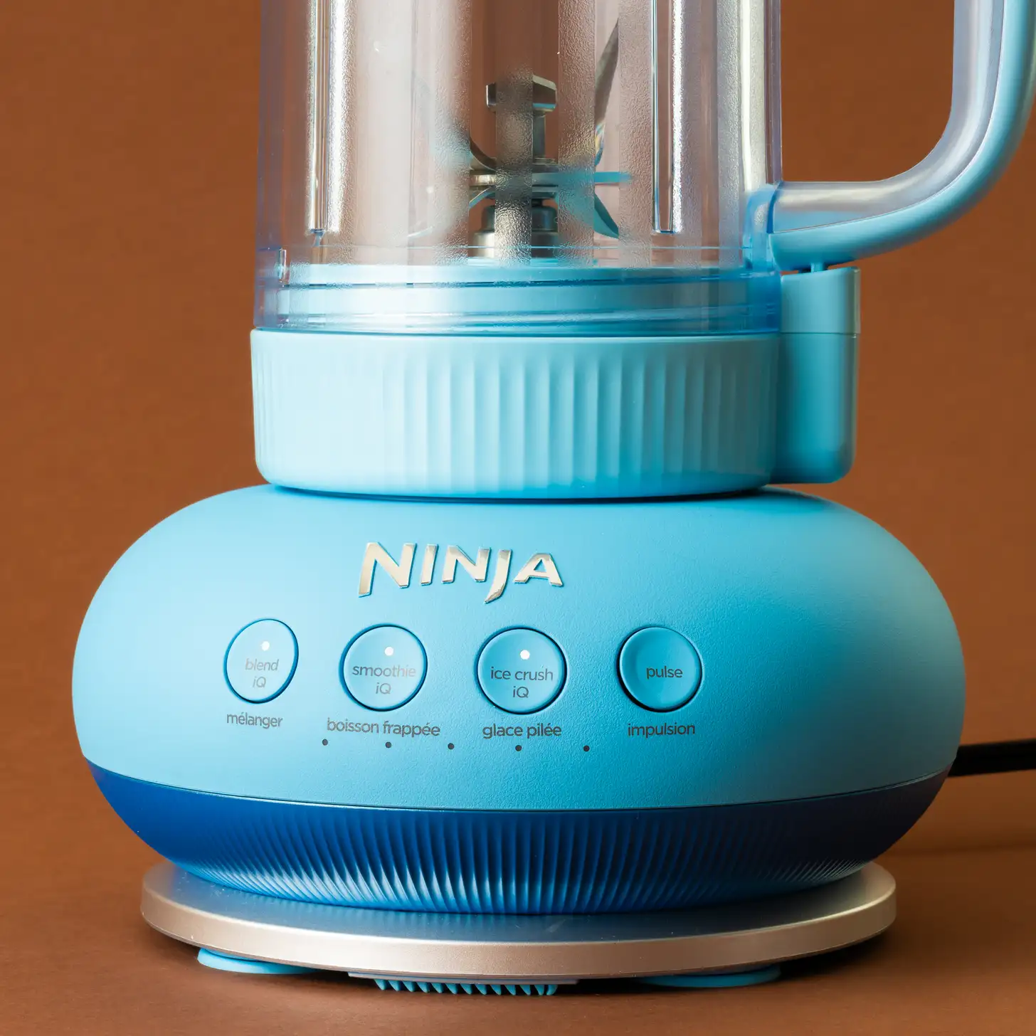 A clean Ninja blender base with buttons and drive spindle in focus, next to a microfiber cloth, cotton swab, and vinegar solution on a kitchen counter.
