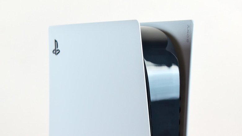 Close-up of a person vacuuming dust catcher ports on a removed PS5 side panel with a brush and toothpick stop for fan blade safety.